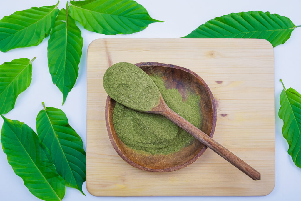 Top view of Kratom powder in wooden bowl and spoon on wooden table, alternative medicine