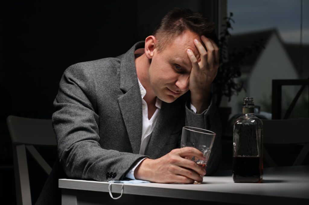 man drinking alcohol in the kitchen after work. Young man suffering from strong headache or migrain